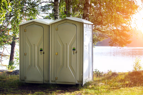 Two luxury restroom trailers sitting near a lake that are available for wedding guests to use.